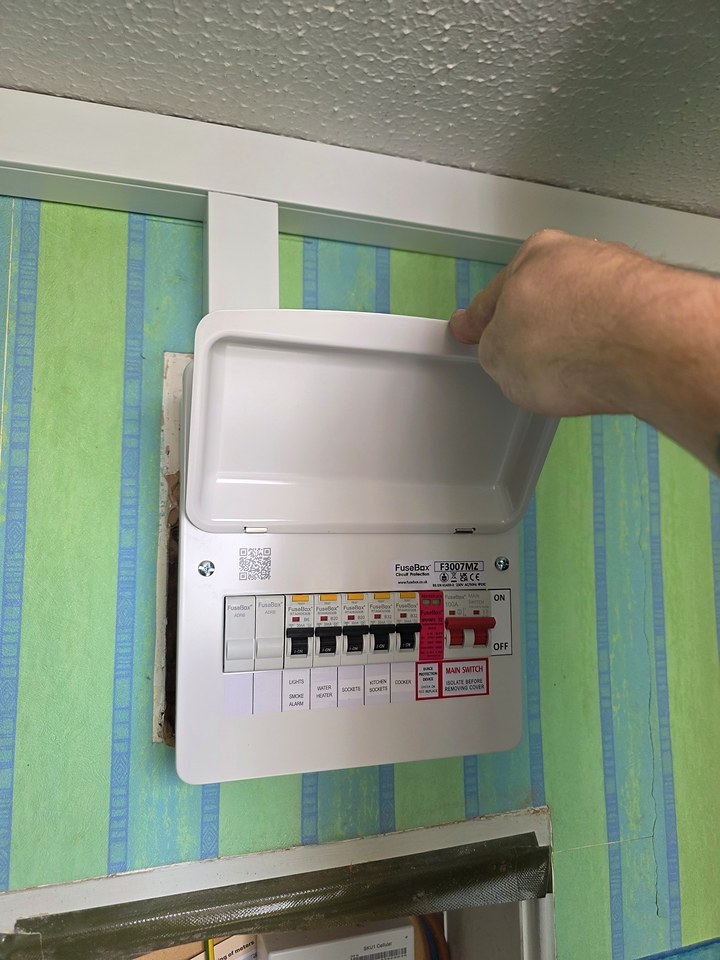 Electrician closing the cover of a new white consumer unit mounted on a striped wall