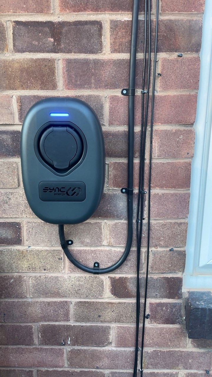 Close-up of a home EV charger on a brick wall with its cables clipped neatly in black conduit