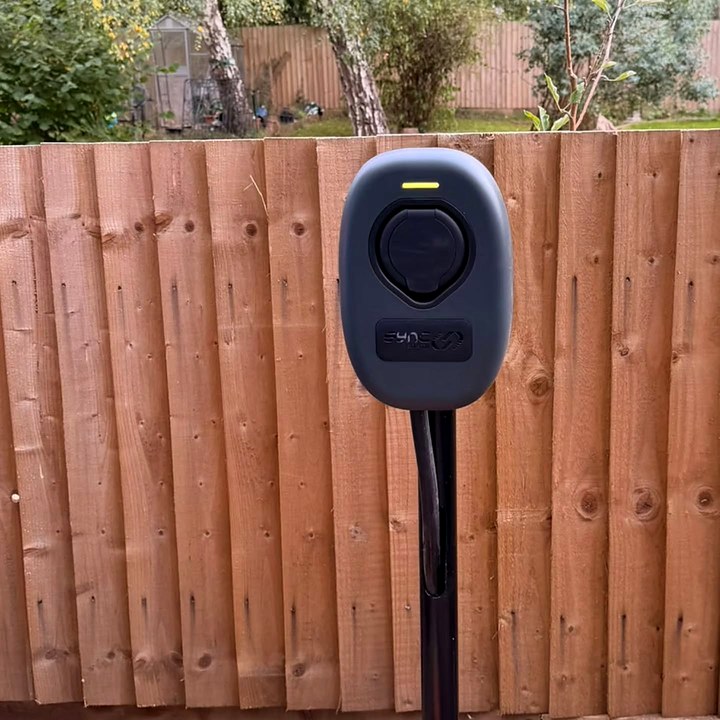 Home EV charger on a black post in front of a wooden garden fence
