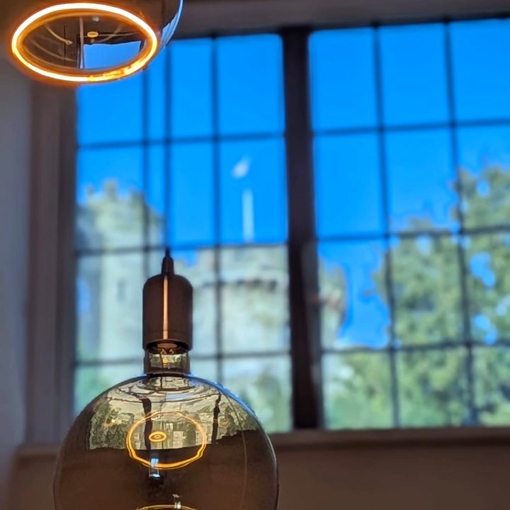 Large globe filament pendant light in front of a leaded window, with Warwick Castle softly out of focus beyond