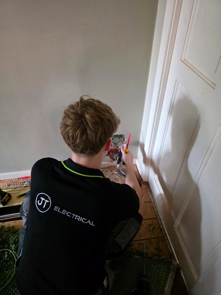 JT Electrical electrician, seen from behind, wiring a socket at skirting level